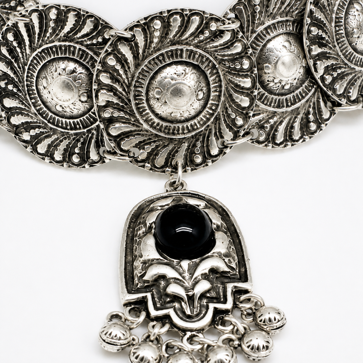 Close-up of the embossed silver-tone disc details and black stone pendant.