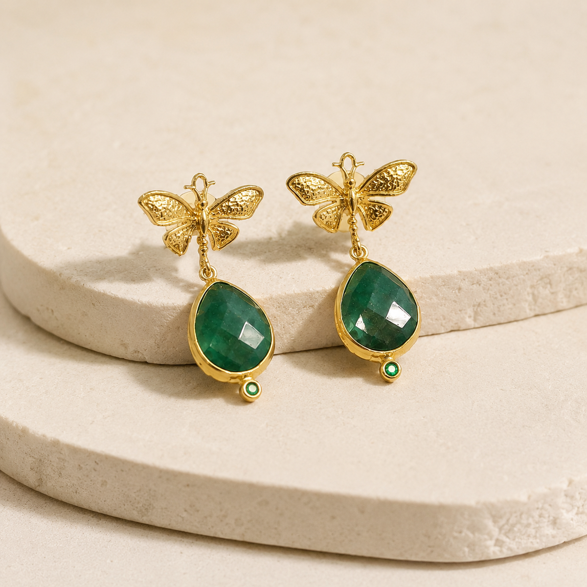 Angle view of gold-plated butterfly earrings with faceted green teardrop drops.