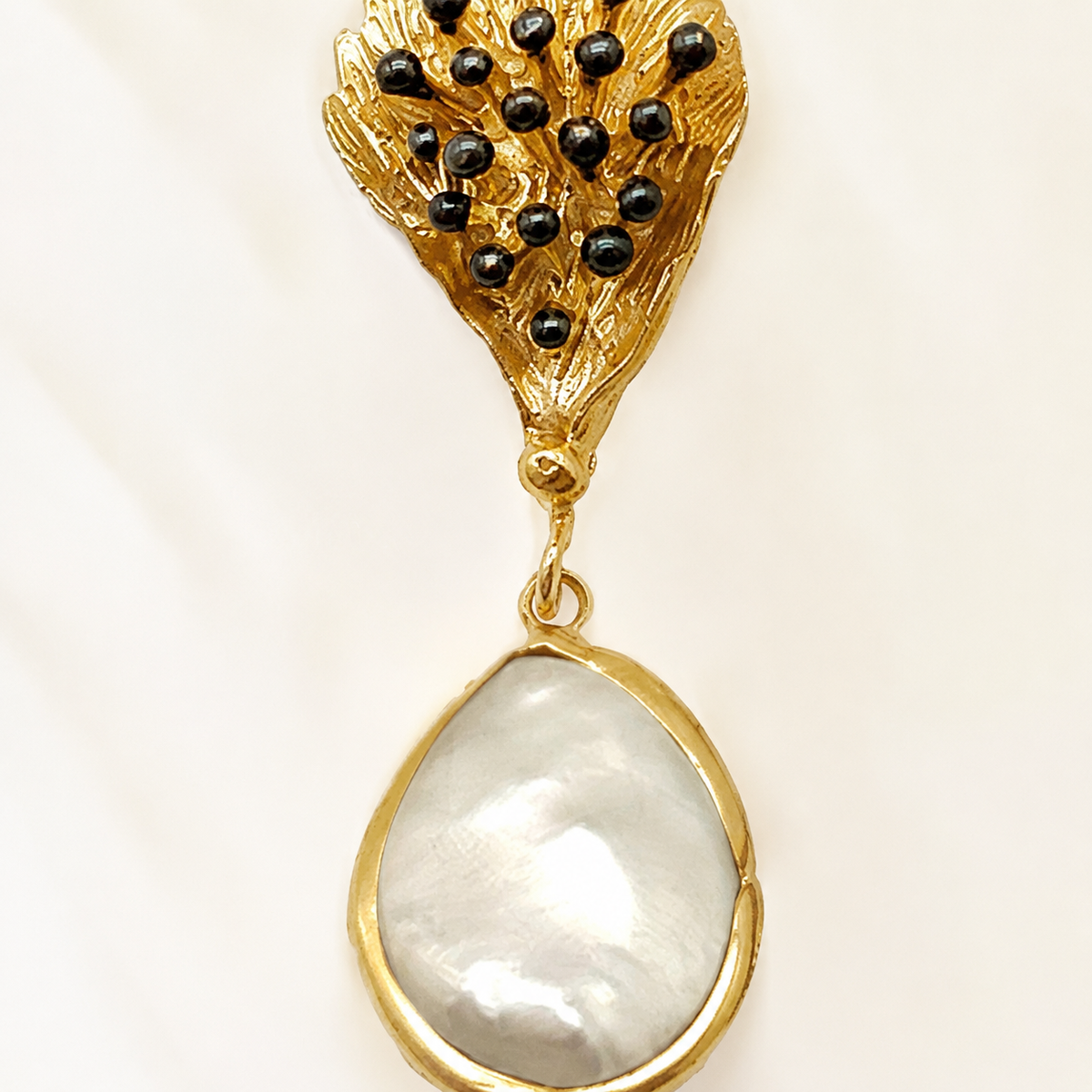 Close view of textured leaf-shaped gold-tone earrings with black bead accents.