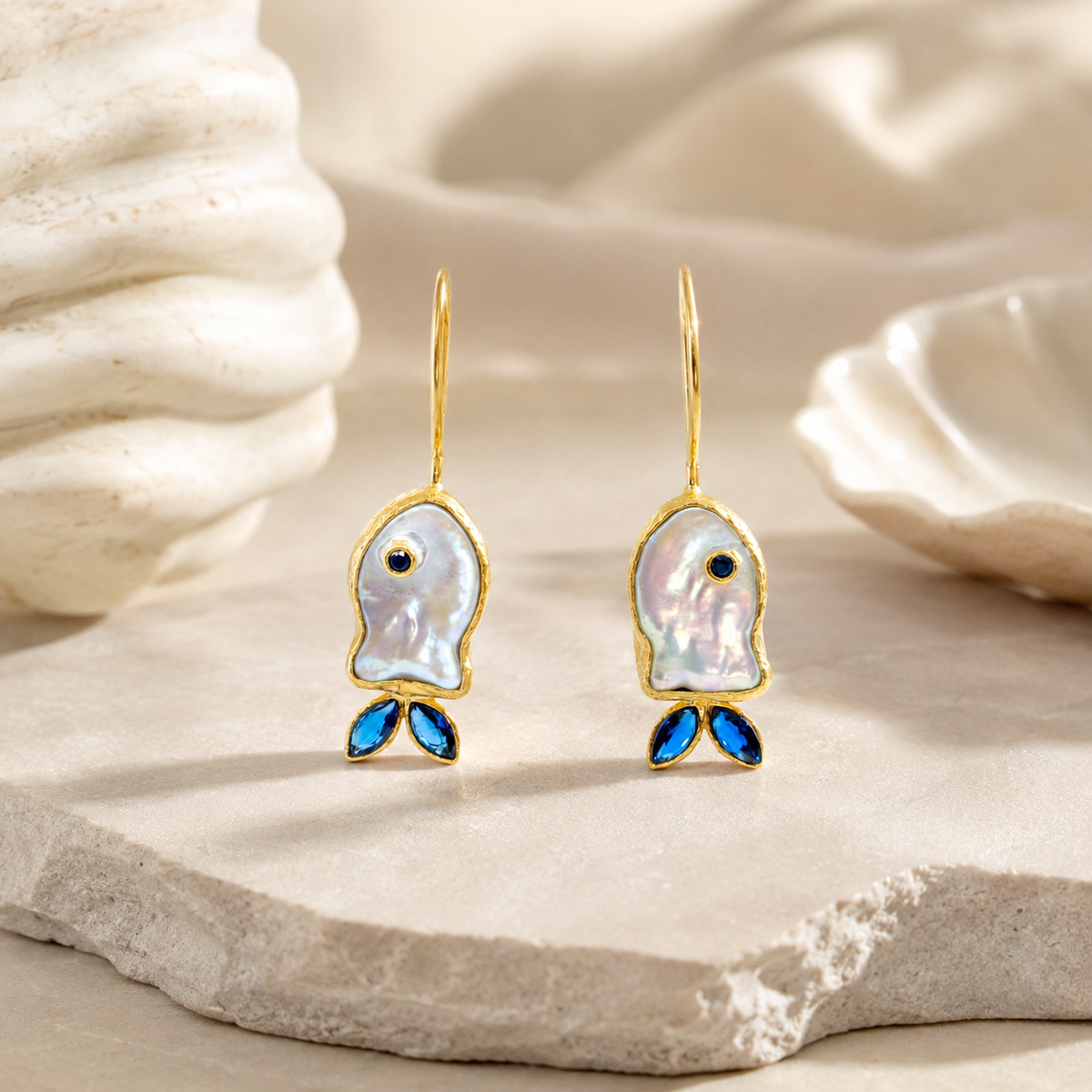 Mother-of-pearl fish drop earrings with blue CZ accents and a gold-plated finish.