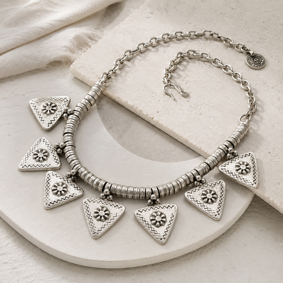 Angled view of a silver-tone triangle flower charm necklace with textured chain links.