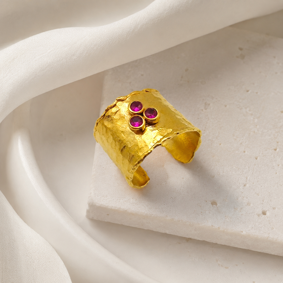 Gold cuff ring with a textured hammered finish and ruby pink stones.