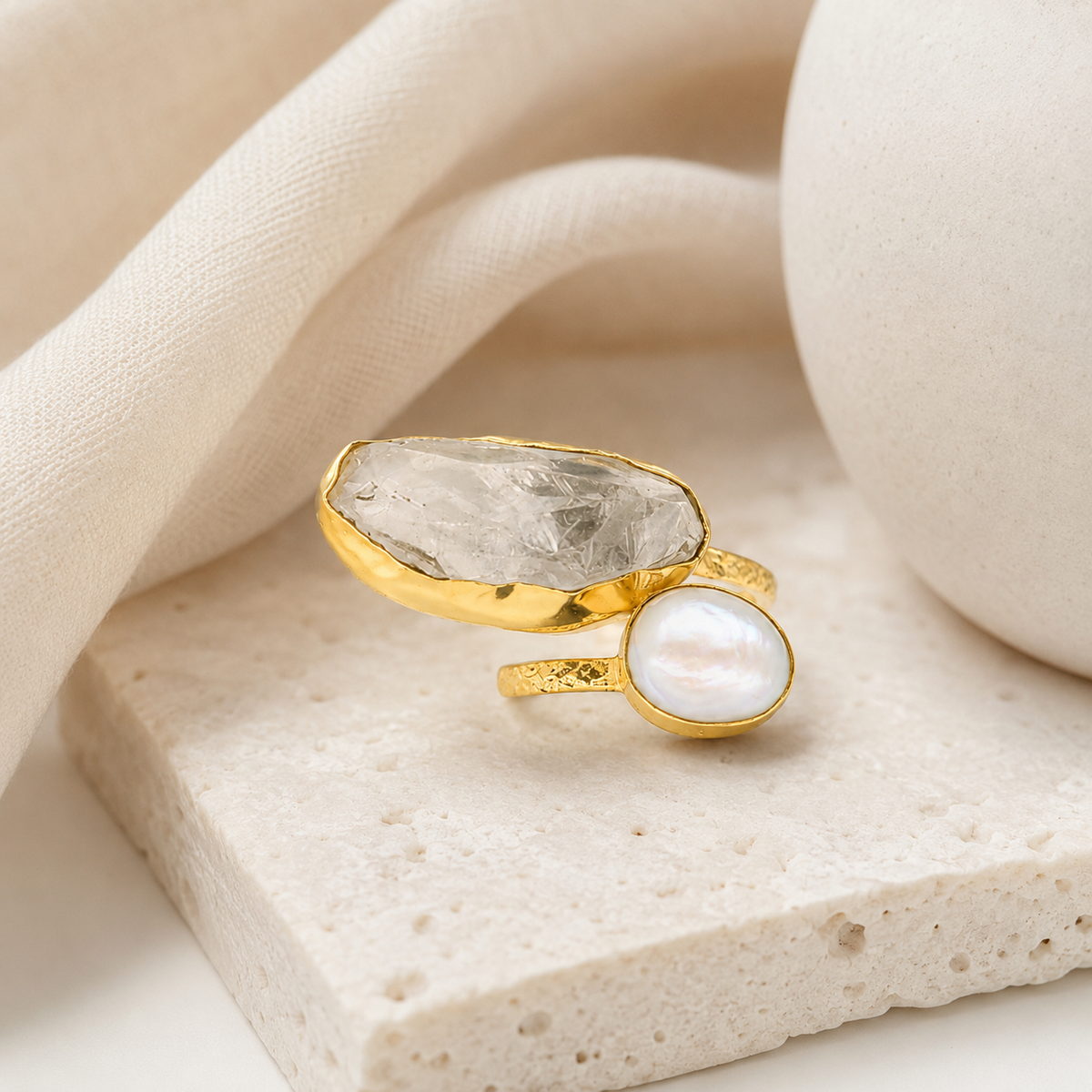 Gold-plated ring with a clear quartz stone and pearl-like accent styled on a white background.