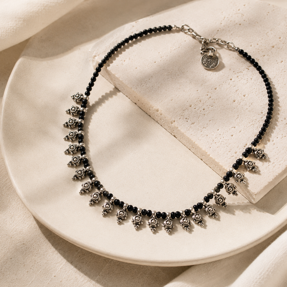 Angled view of a black bead necklace with silver-tone dangle details.