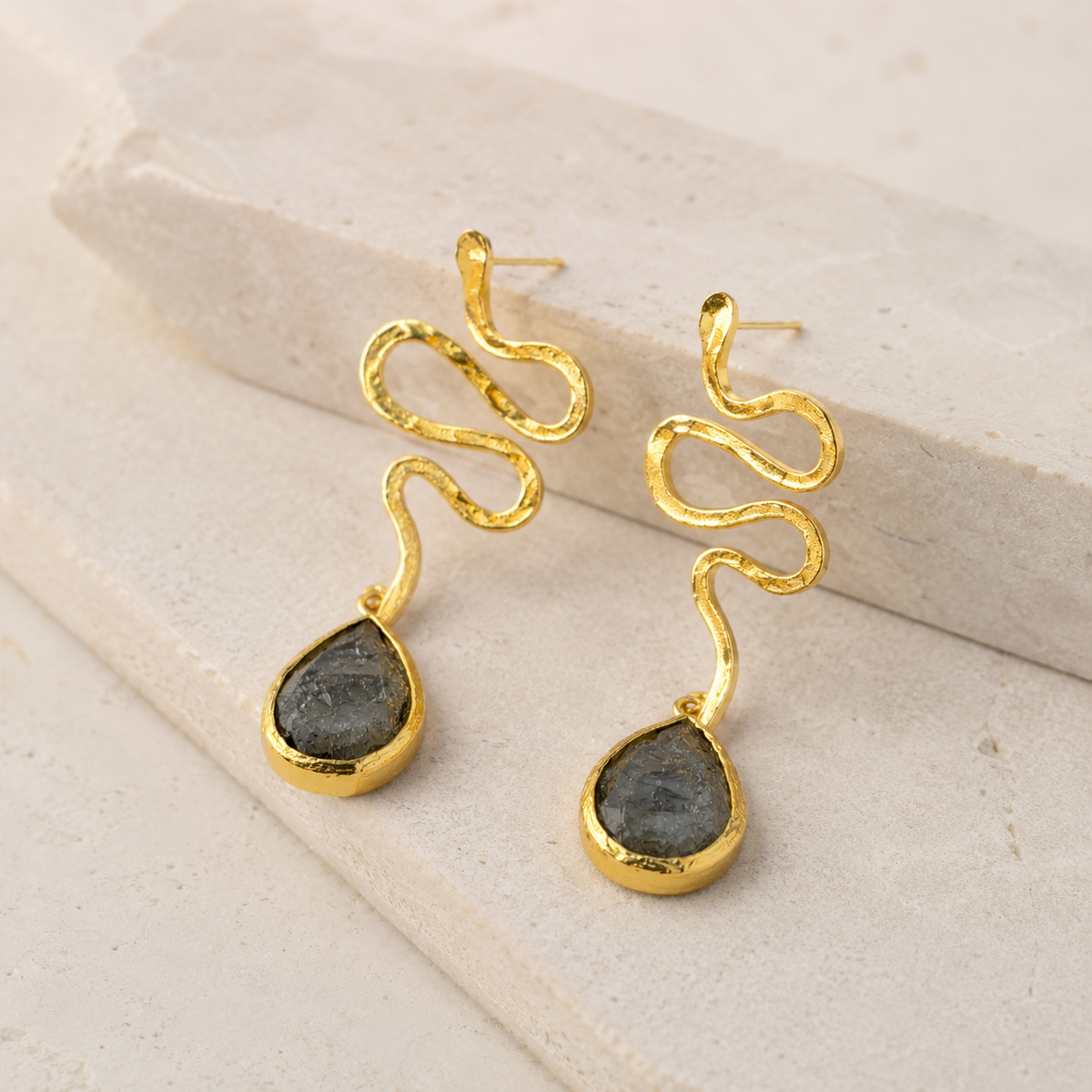 Angle view of gold-plated snake shape dangle earrings with teardrop accents.
