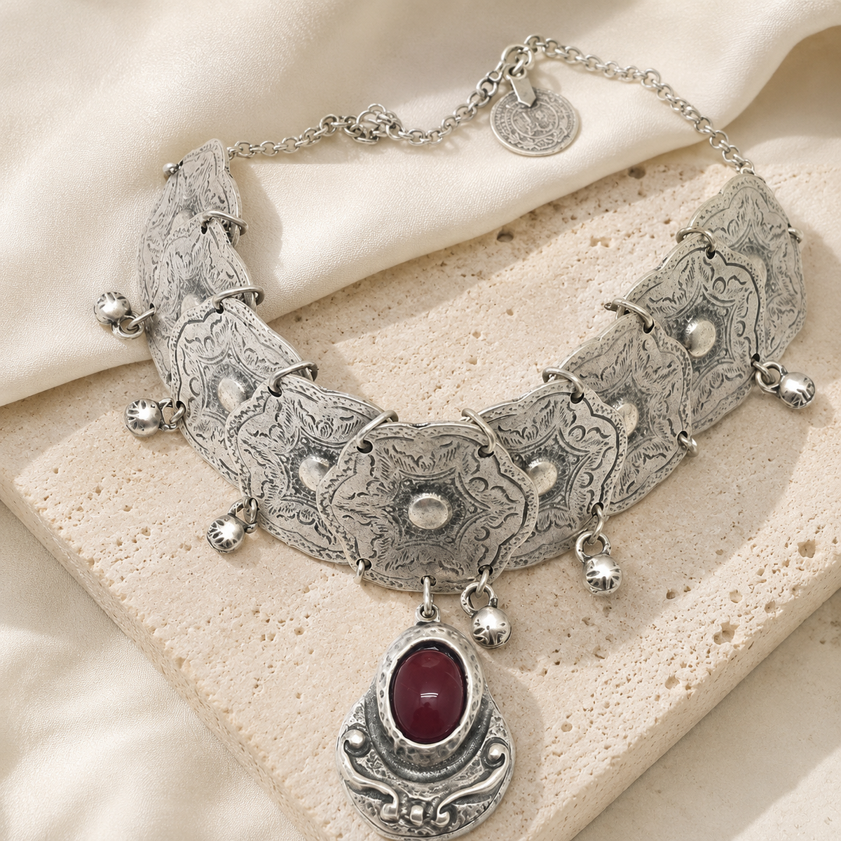 Angled view of a silver-tone choker necklace with engraved plates and red stone detail.