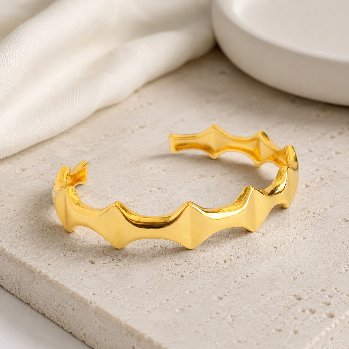 A gold-tone open cuff bracelet resting on a soft neutral surface.