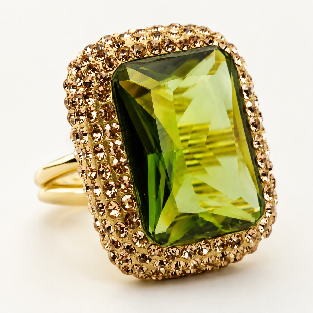 The ring shows a faceted green center stone with a textured gold-tone border.