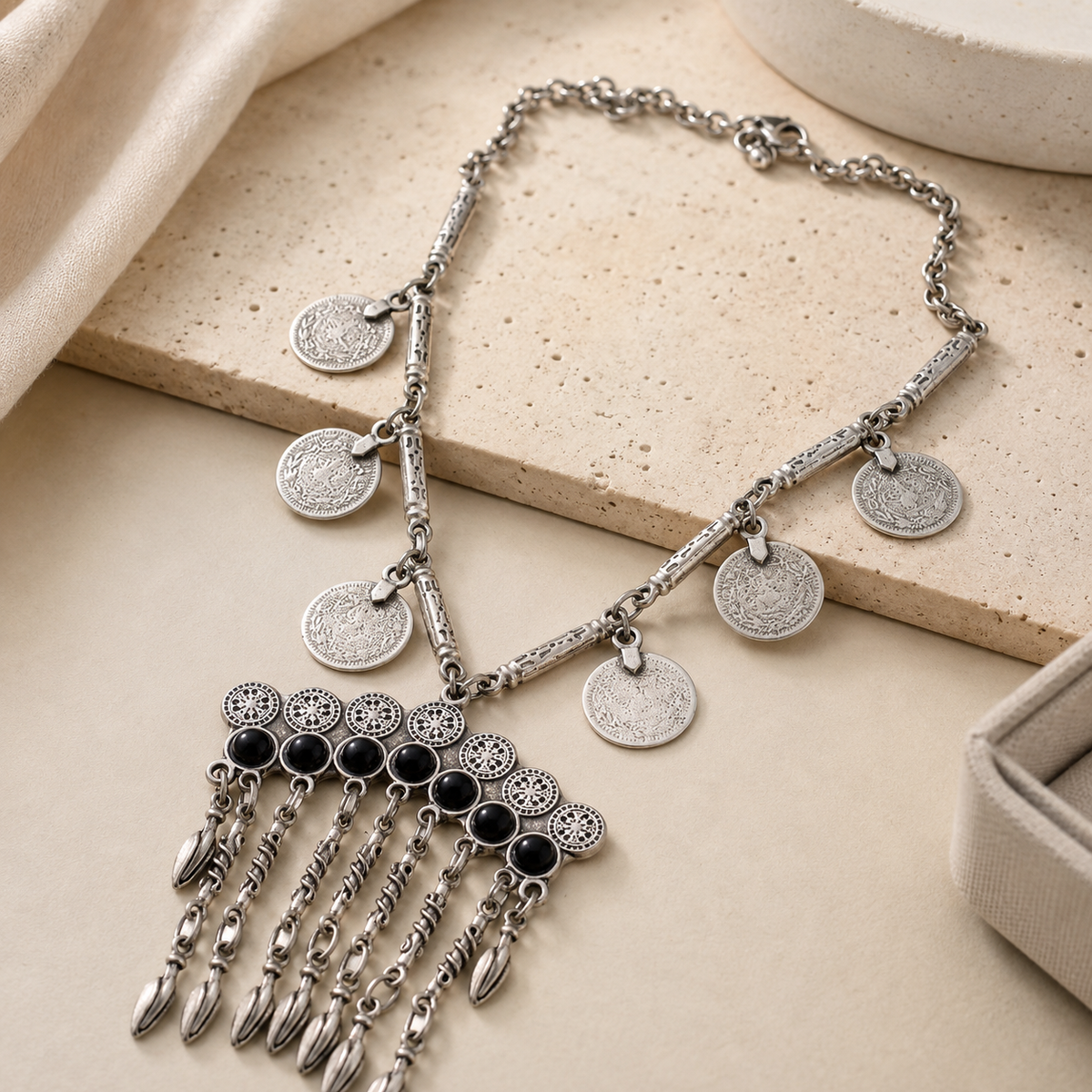 Angled view of a silver-tone bib necklace with coin charms and black stone accents.