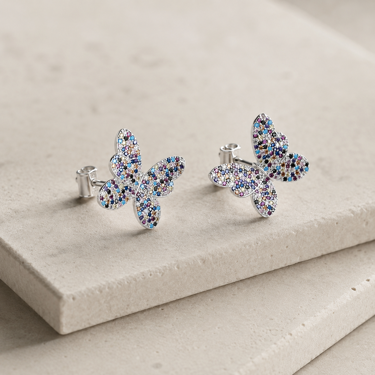 Angled view of butterfly stud earrings with multicolor CZ sparkle and silver-tone edges.