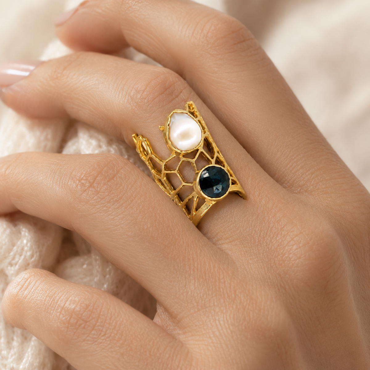 Gold-plated statement ring with honeycomb openwork and two contrasting stones on a display stand.