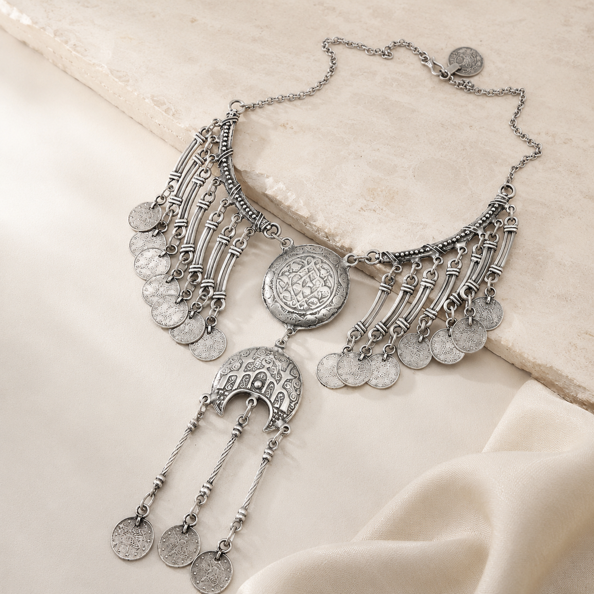 Angled view of a silver-tone crescent necklace with layered coin charms.