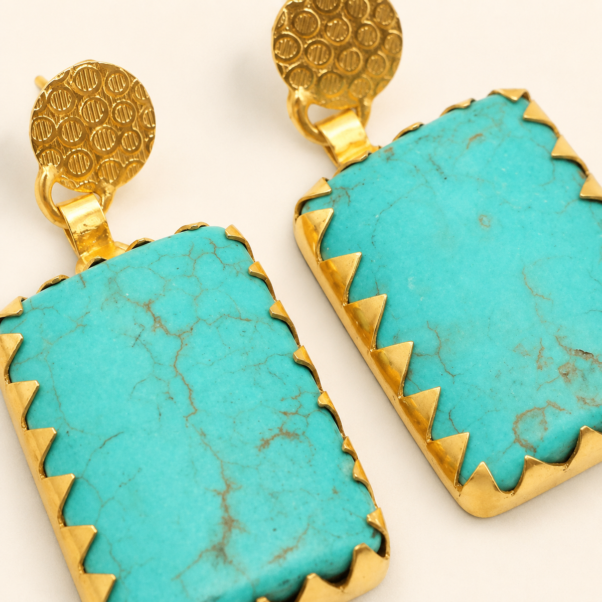 Close-up of turquoise statement earrings showing gold-plated edges and textured detailing.