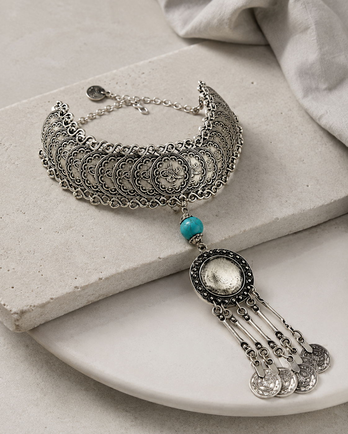 Angled view of a silver-tone coin choker necklace with textured details.