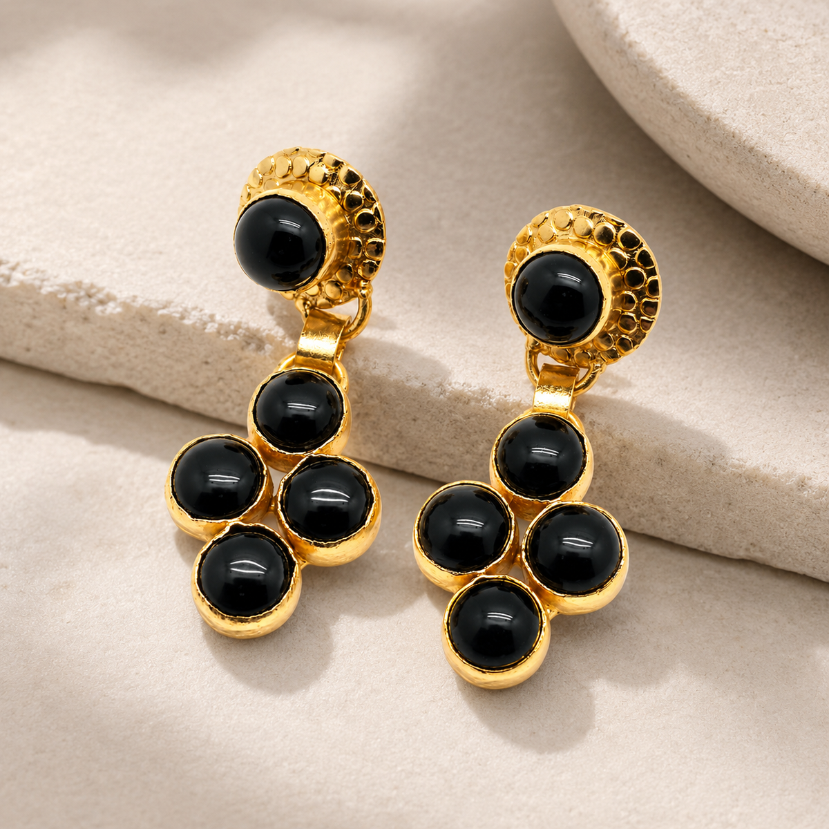 Angle view of gold-plated dangle earrings with glossy black onyx stones.