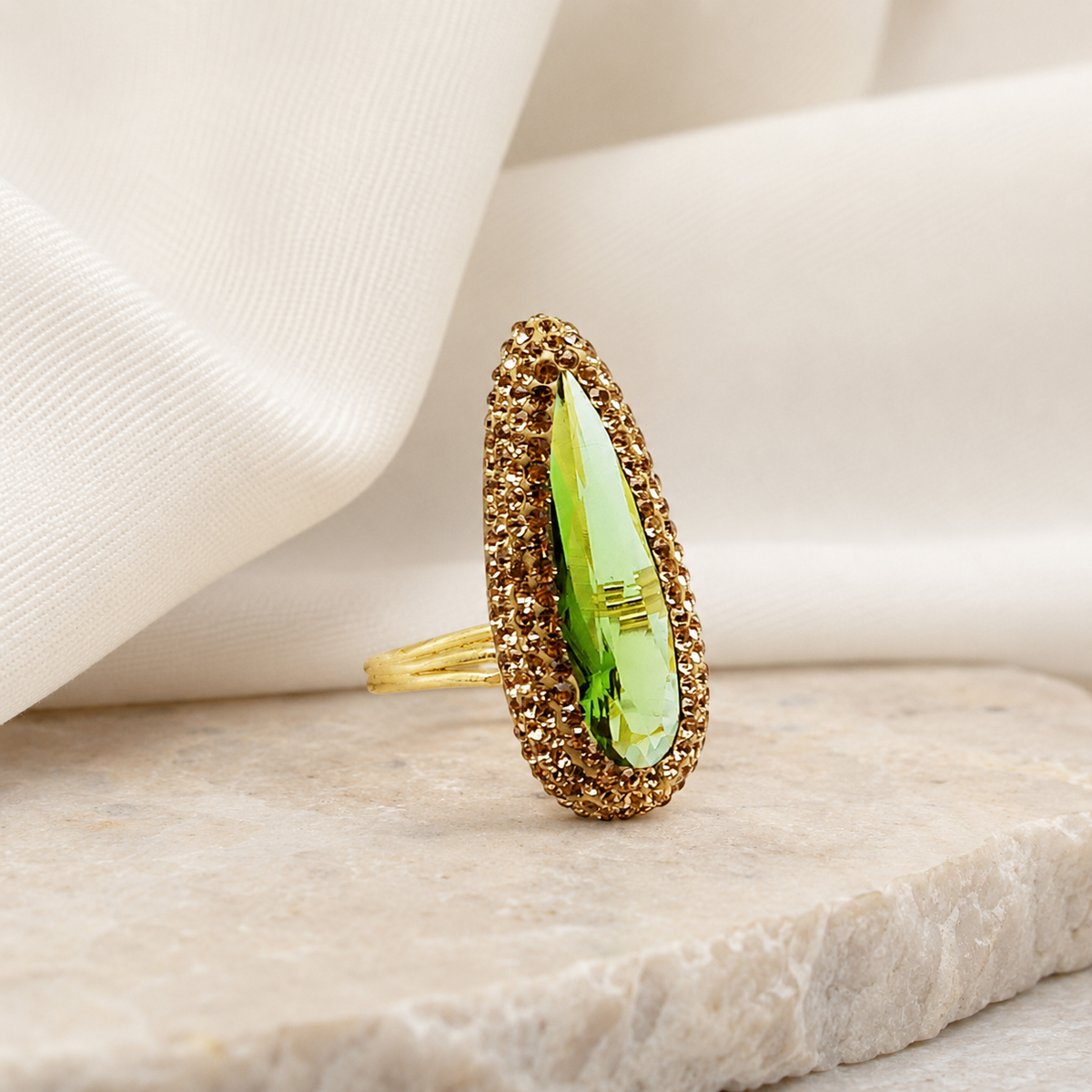 Gold-tone statement ring with a bright green stone on a white background.