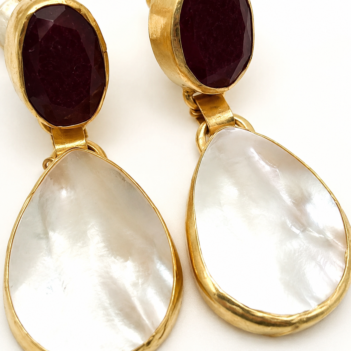 Close view of red garnet and mother of pearl drop earrings with a gold finish.
