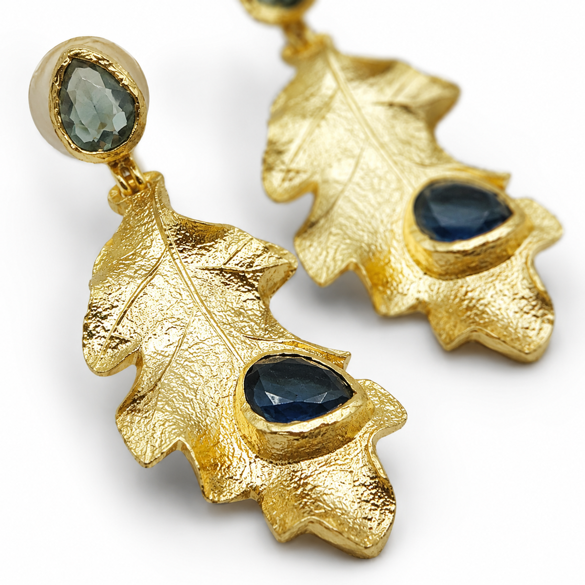 Close view of textured gold leaf earrings with blue stone details.