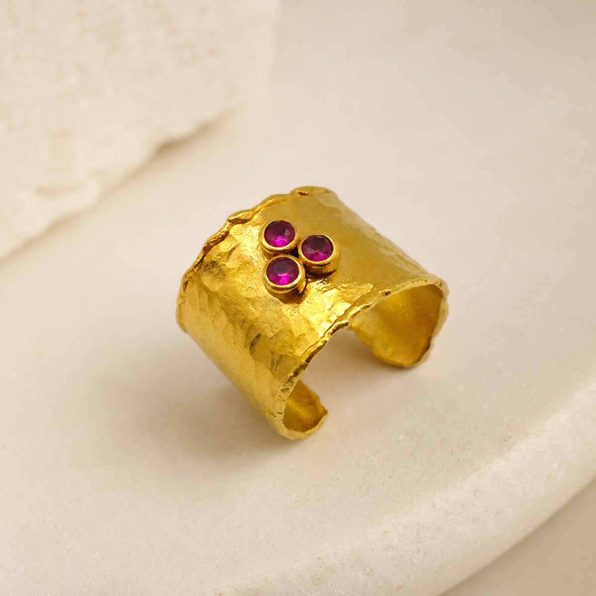 Angled view of a hammered gold-plated cuff ring with three ruby pink stones.