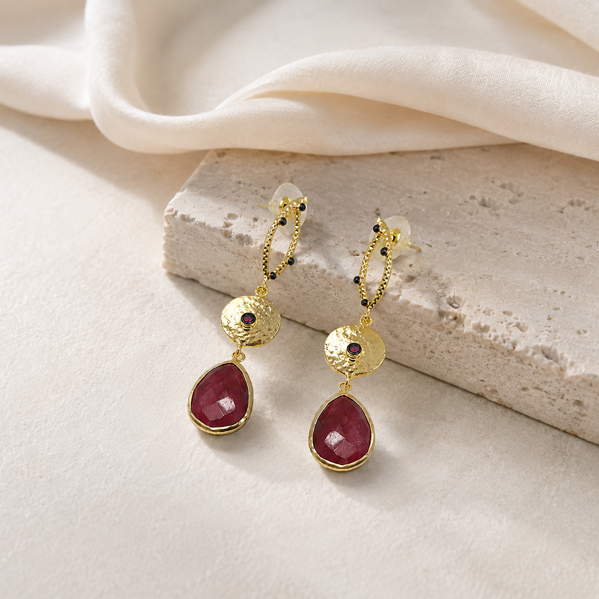 Long gold-plated statement earrings with red faceted drops styled for a polished look.