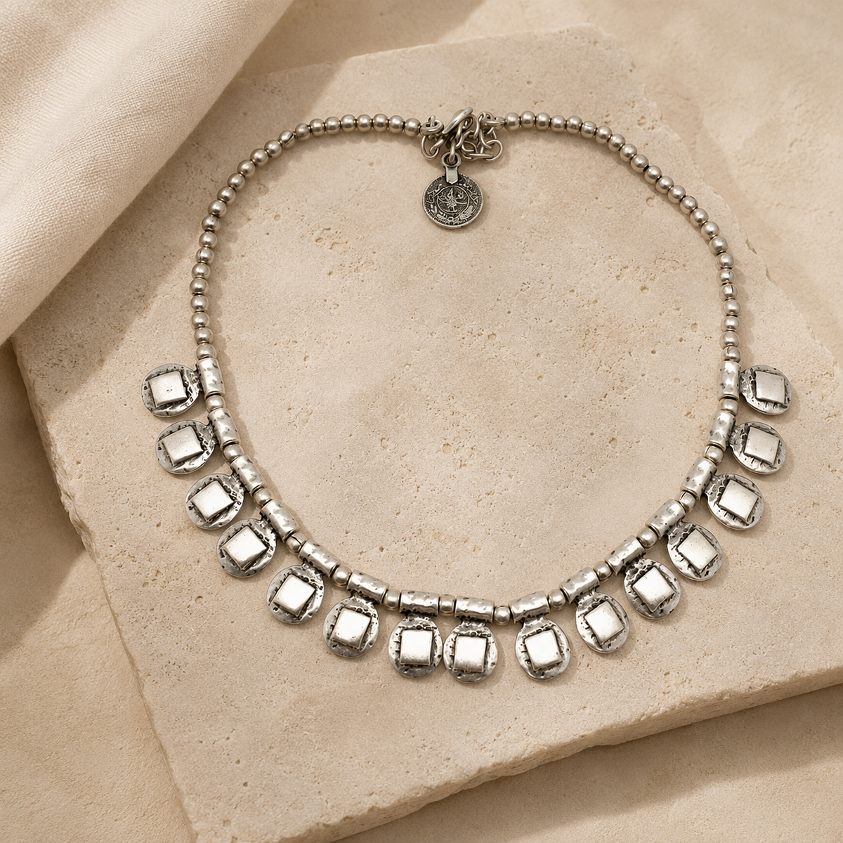 Silver-tone necklace with beaded chain and square drop accents on a white background.