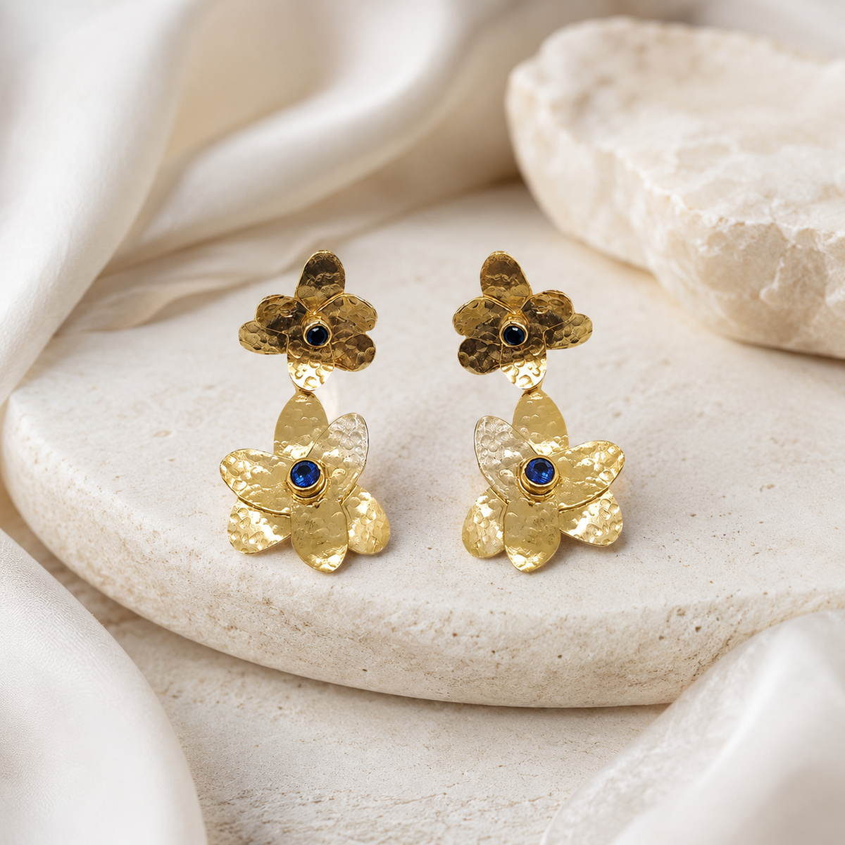 Gold flower drop earrings with blue stone centers and a textured finish.