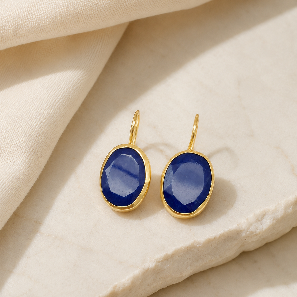 Gold-plated drop earrings with deep blue stones on a white background.