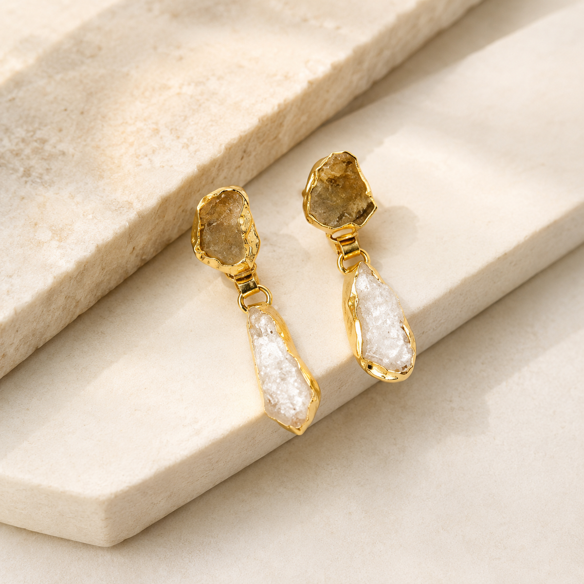 Angle view of gold-plated drop earrings with rough citrine and clear quartz stones.