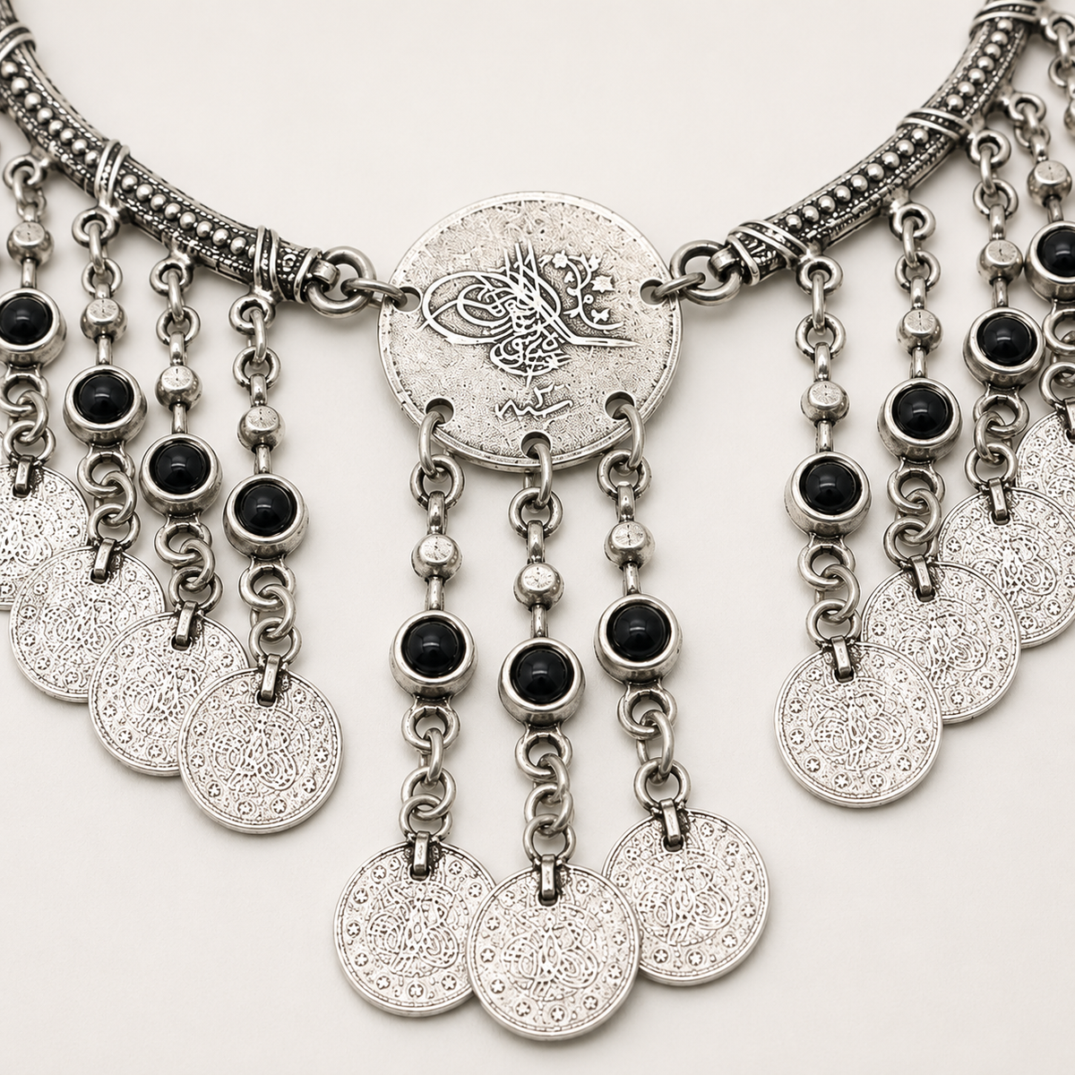Close view of the antique silver necklace with textured coin and black stone details.