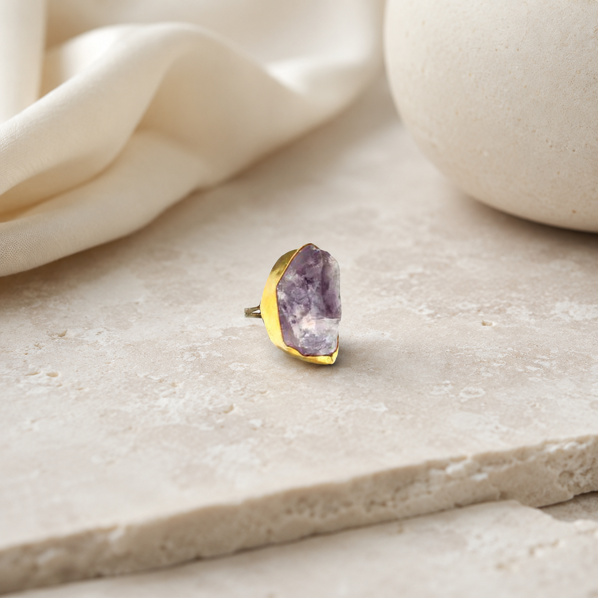 Gold-plated statement ring with a raw amethyst stone on a white background.