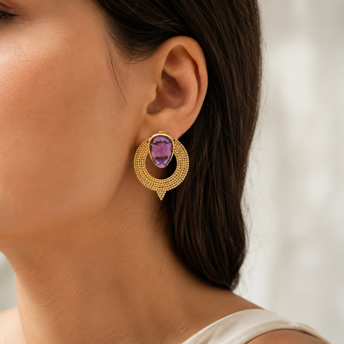 Pair of gold-plated earrings with purple CZ stones and a circular textured design.