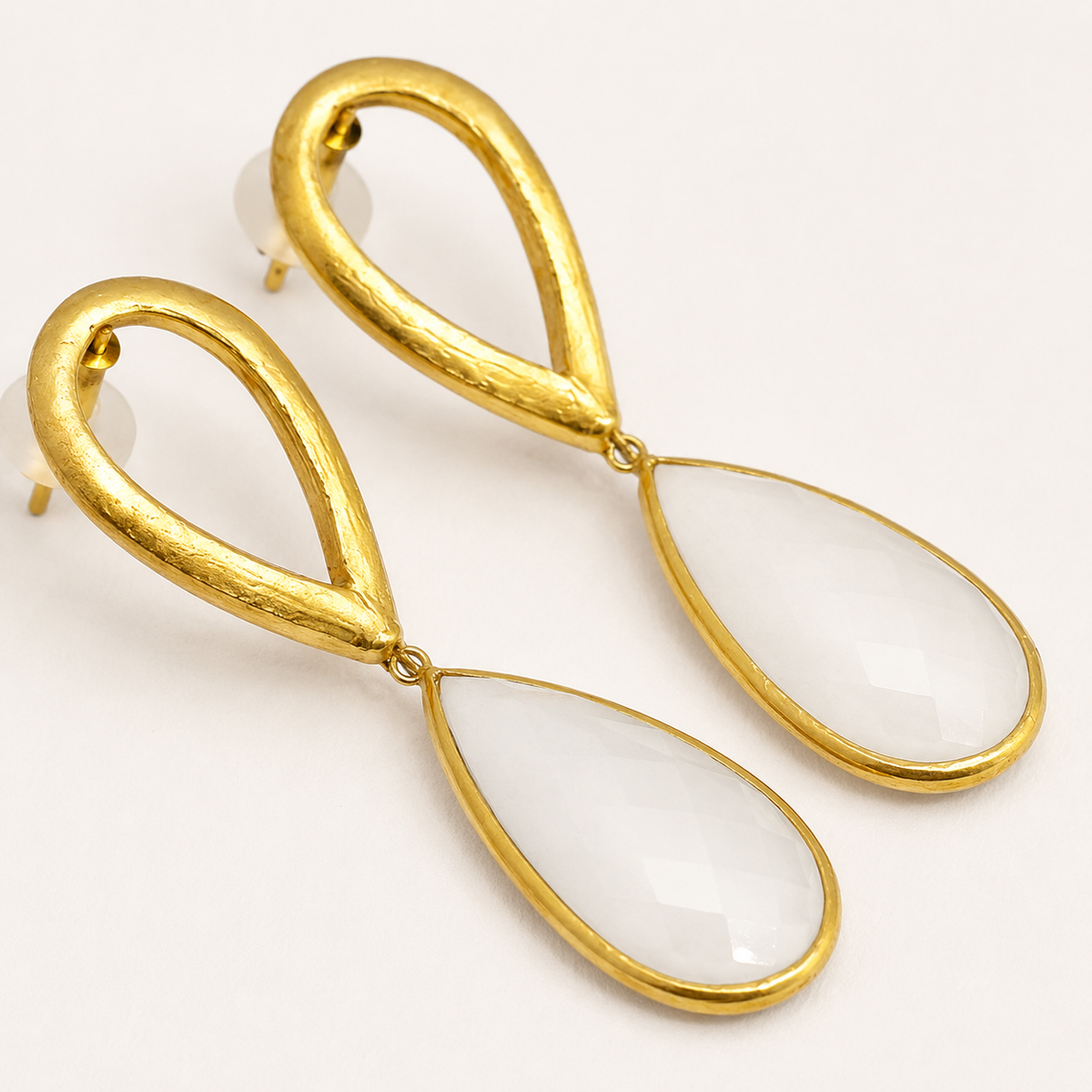 Close view of hammered gold-plated earrings with clear teardrop drops.