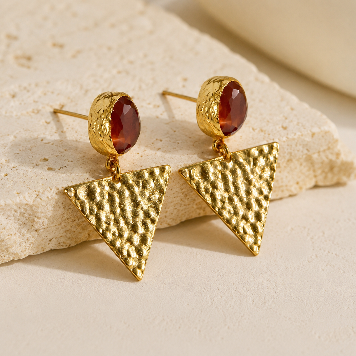 Angle view of orange triangle gold plated drop earrings with a faceted stone and textured finish.