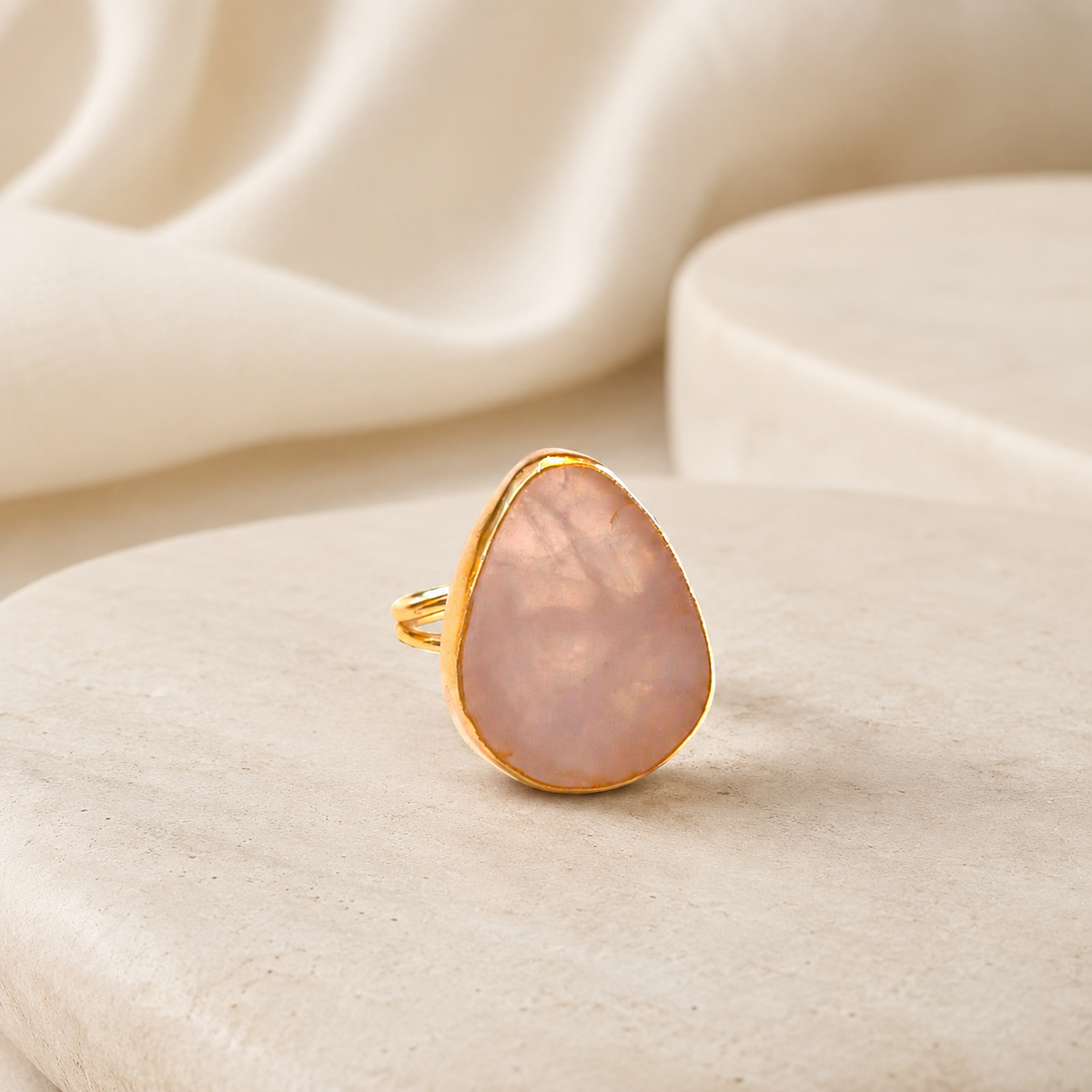 A rose quartz statement ring with a smooth teardrop shape and gold finish.