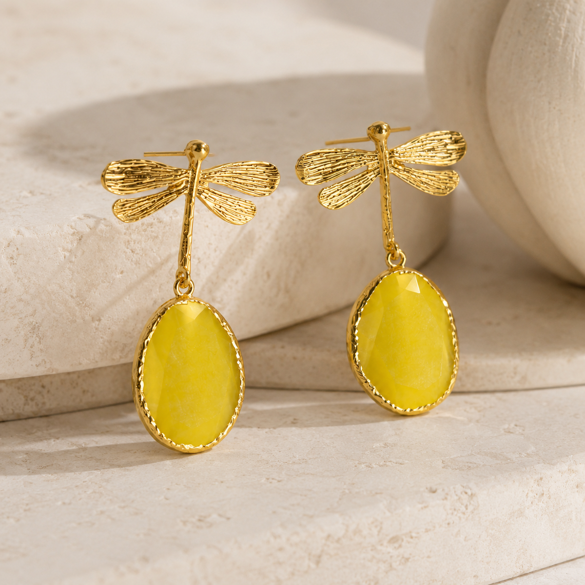 Angled view of gold dragonfly drop earrings with textured wings and oval drops.