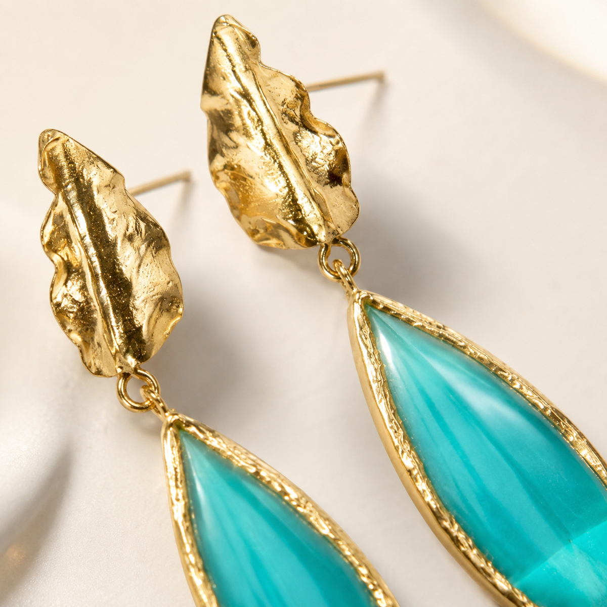 Close-up of gold-plated leaf drop earrings with pine green teardrop accents.