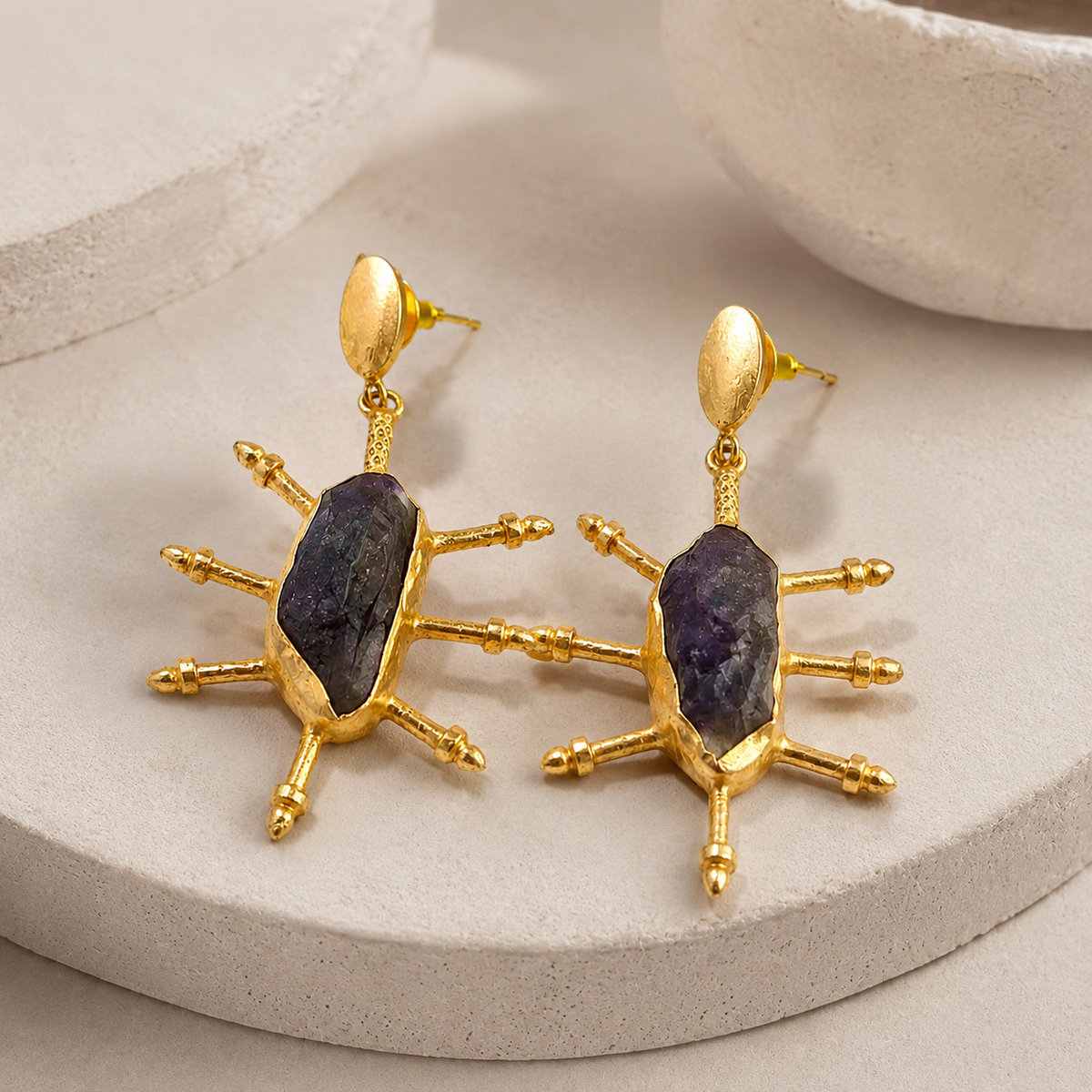 Angled view of raw amethyst statement earrings with gold-plated spikes.