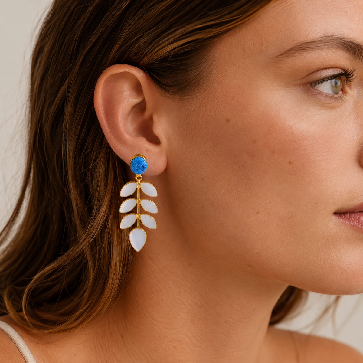 Front view of gold-plated earrings with bright blue druzy and layered mother of pearl leaf details.