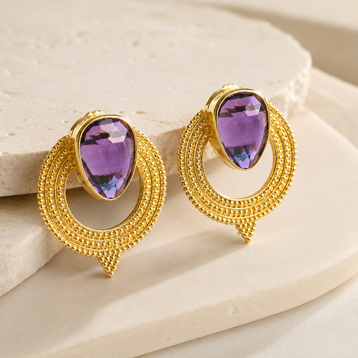 Angle view of gold-plated earrings with purple CZ stones and textured circular frames.