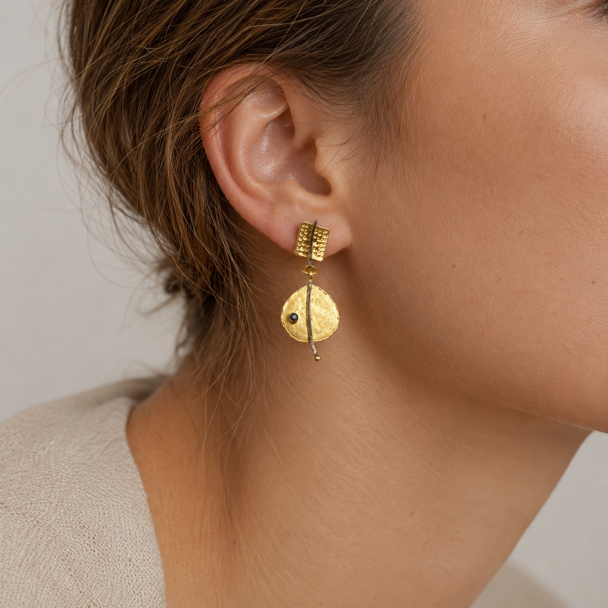 A pair of gold-plated earrings with textured discs and a slim vertical drop.