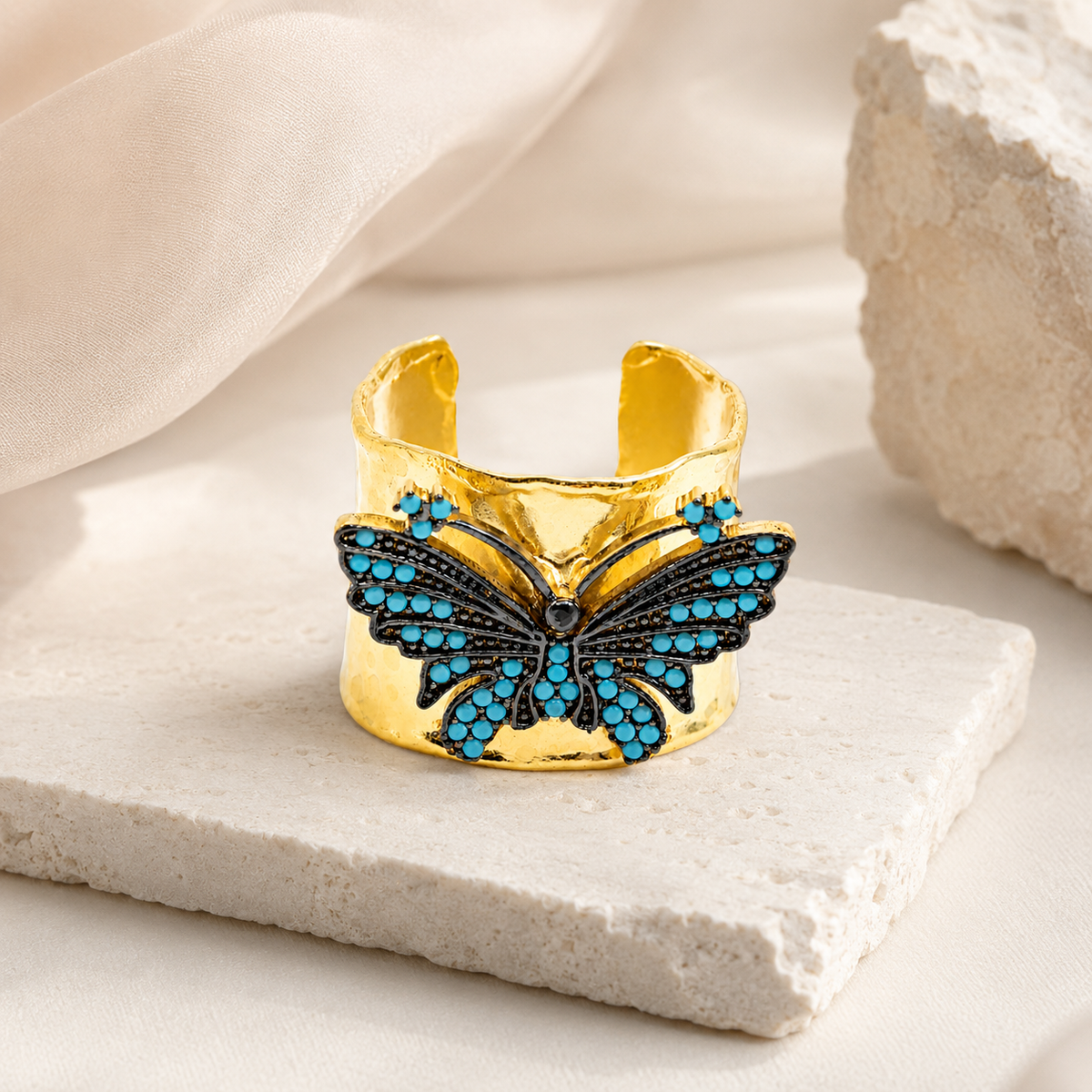 Gold-plated butterfly cuff ring with turquoise blue details on a white background.