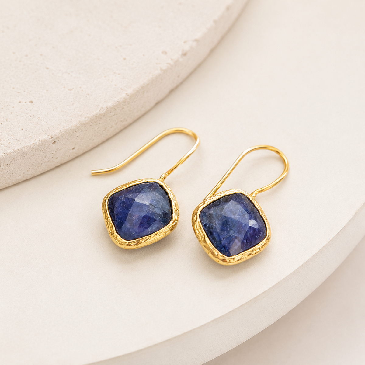 Angle view of blue sapphire dangle earrings with a gold-plated frame.