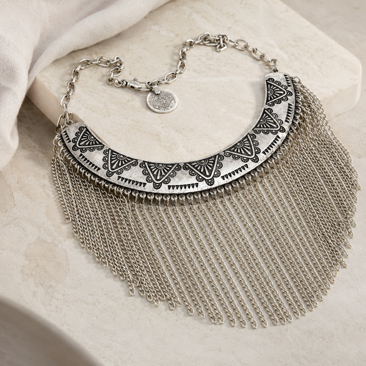 Angled view of a silver-tone engraved collar necklace with chain fringe.
