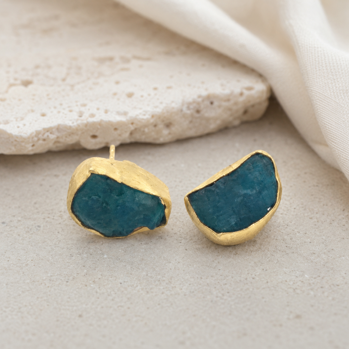 Gold-plated stud earrings with rough blue apatite stones on a white background.