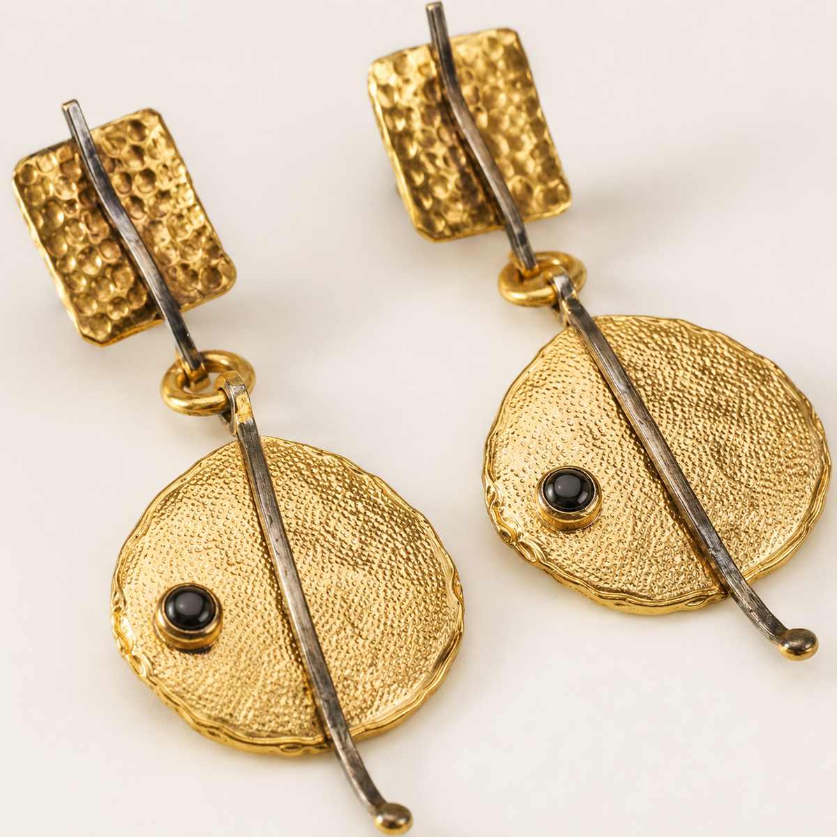 Close view of hammered gold-plated earrings with a small black bead detail.