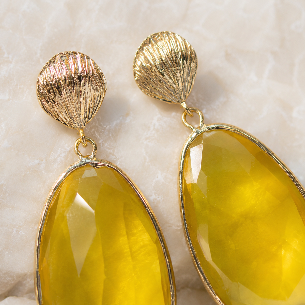 Close view of gold-tone earrings with a textured shell top and faceted yellow cat eye stone.