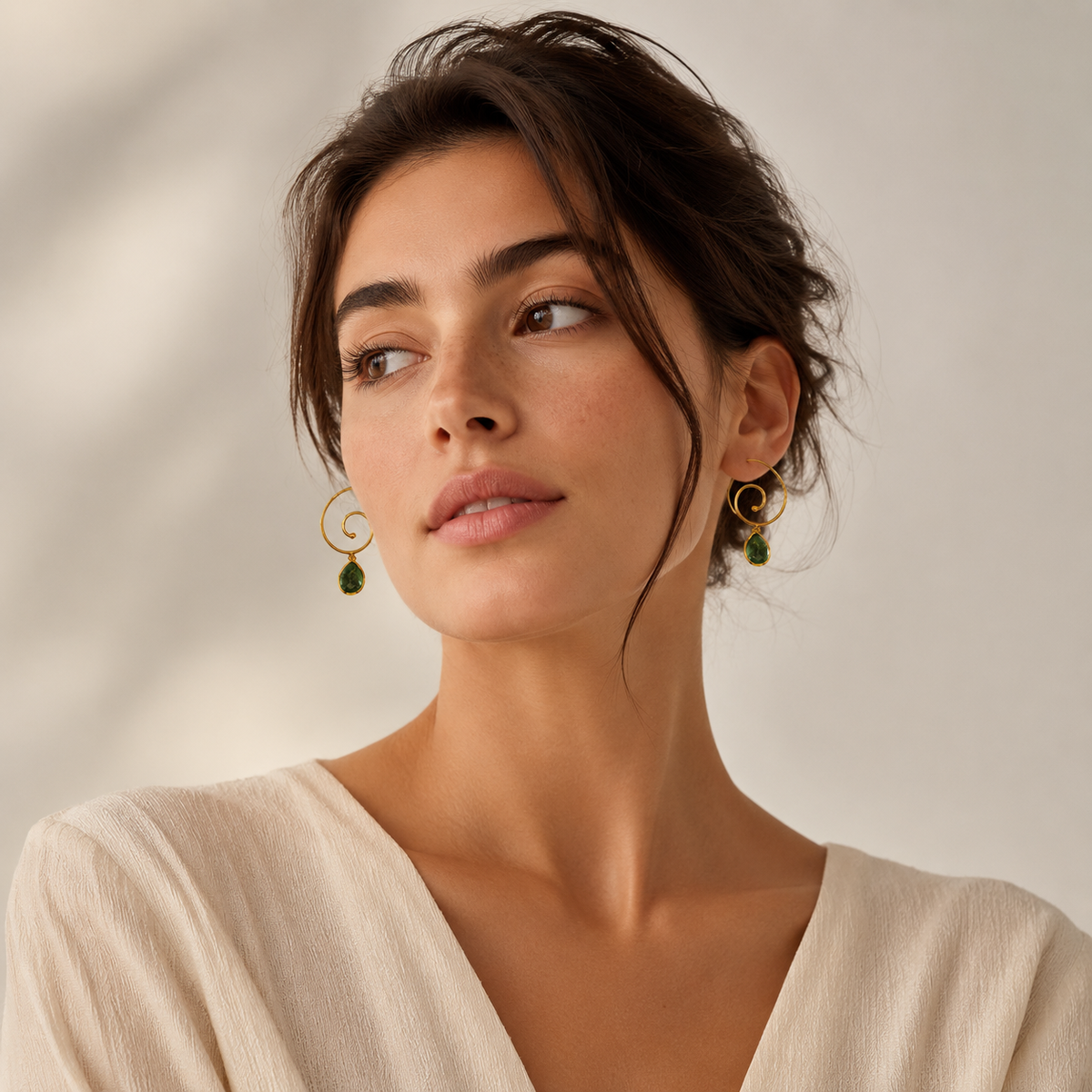 Gold spiral earrings with green teardrop accents displayed on white.