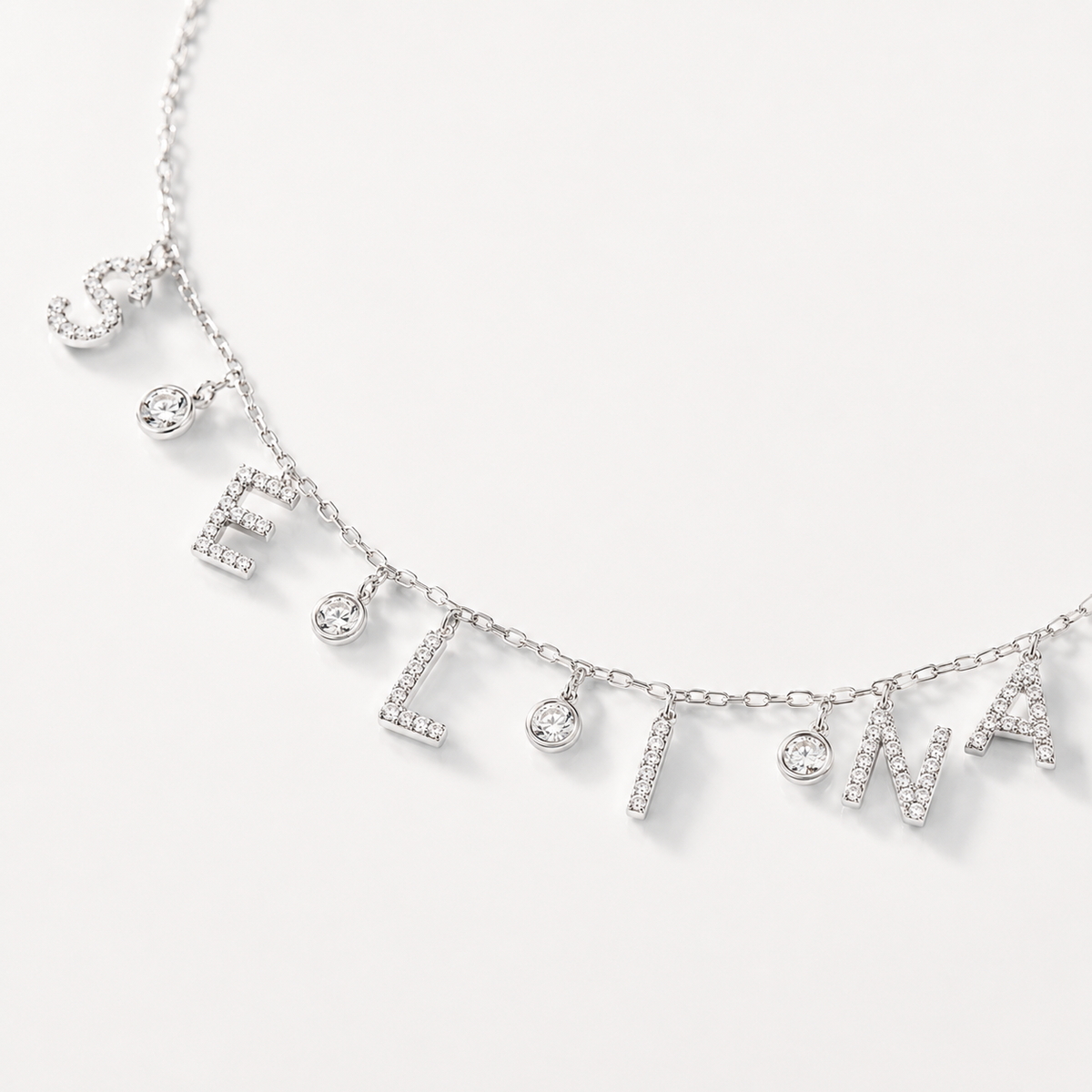 Close view of sparkling letter charms and small drop details on a delicate necklace.