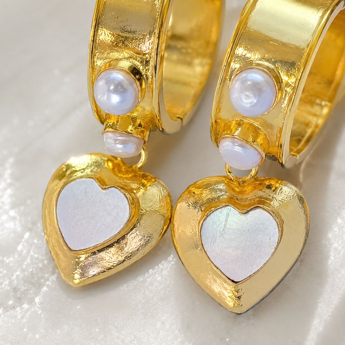 Close view of gold-plated earrings with heart-shaped mother of pearl charms.