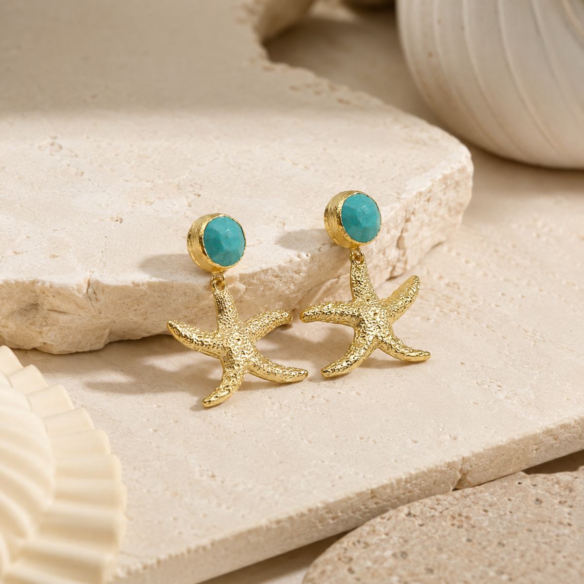Angled view of gold-plated starfish drop earrings with turquoise round stones.